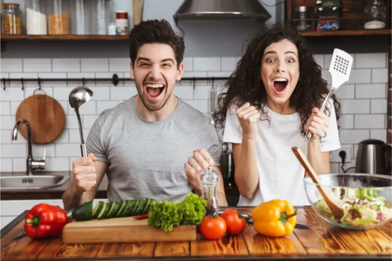Excited cheerful young couple cooking healthy salad