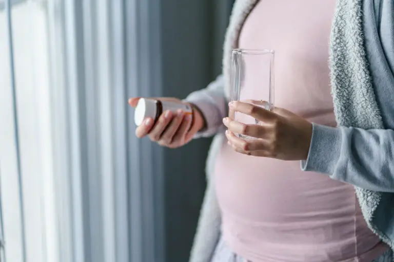 Close up on midsection of unknown caucasian woman pregnant mother holding medicine supplement drugs and glass of water - taking vitamins during pregnancy concept