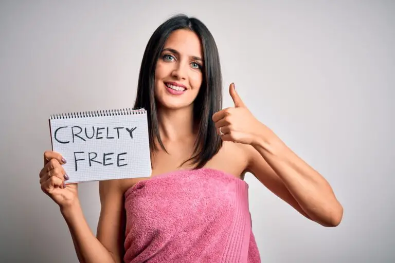 Young brunette woman with blue eyes holding paper with cruelty free message happy with big smile doing ok sign, thumb up with fingers, excellent sign