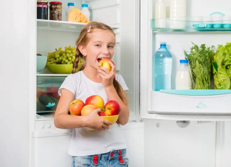 little girl biting apple near fridge