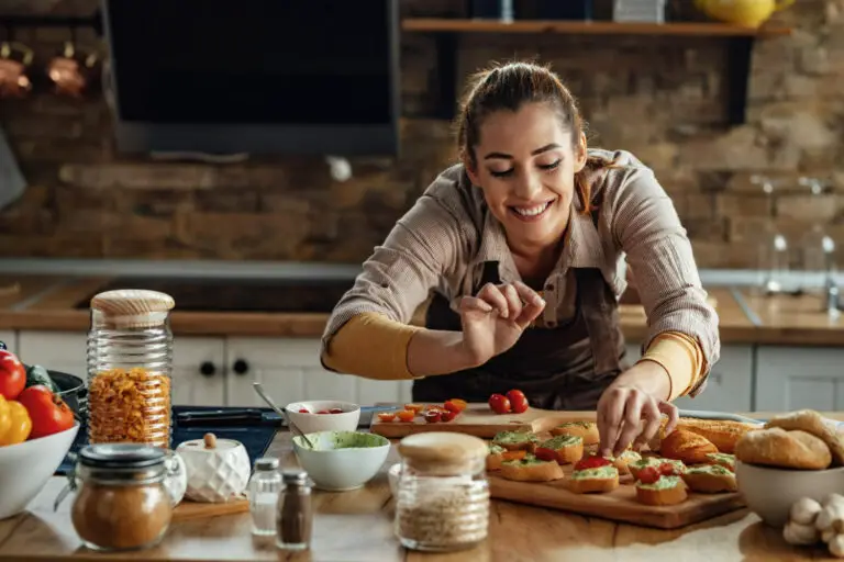 young-smiling-woman-making-bruschetta-with-healthy-ingredients-while-preparing-food-kitchen (1)