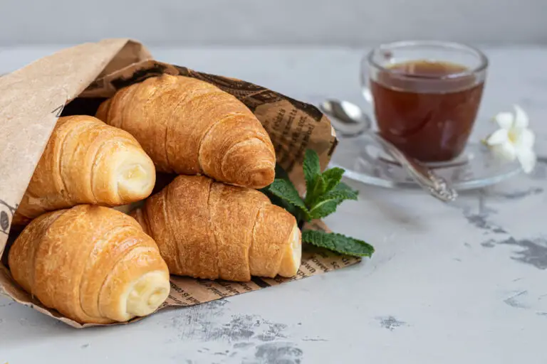 Croissants and coffee for breakfast with fresh raspberry jam on a light background. Decorated with a sprig of mint