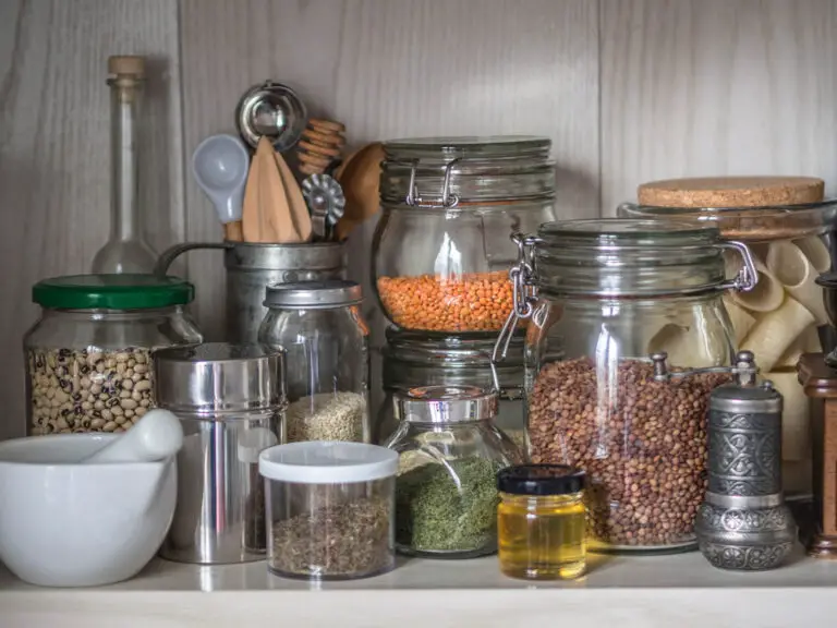 Shelf in the kitchen with various jars of cereals and kitchen tools. Glass jars with pasta, lentils, couscous, beans and quinoa. Coffee grinder, honey, spices, herbs, sesame on shelf