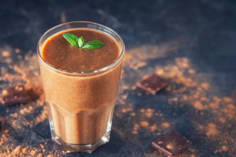 Chocolate smoothie with banana, decorated with mint leaf on the dark background with pieces of chocolate and cocoa powder. Healthy diet food. Selective focus, space for text